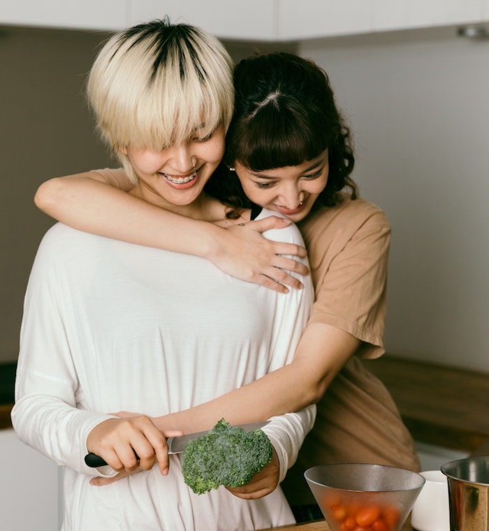 two woman hugging and cutting vegetables